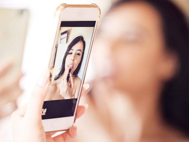 Este espejo funciona para mí. Una foto de una hermosa joven que usa su teléfono como espejo mientras se aplica lápiz labial en casa.