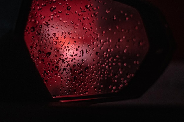 Espejo retrovisor de un coche lleno de gotitas de agua, reflejando la luz de freno