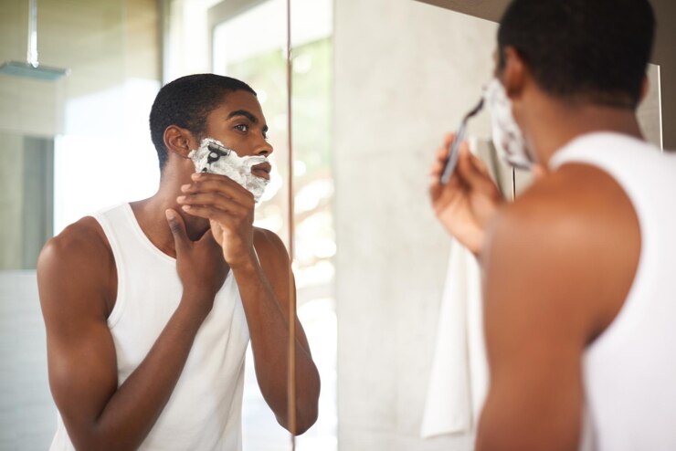 Foto espelho de barbear ou cuidados com o cabelo e homem preto no banheiro da casa com uma navalha para depilação matinal cuidados com a pele do rosto e reflexo de jovem com espuma para barbear barba para rotina de higiene