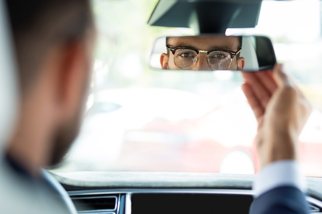 Espelho de fixação. jovem empresário usando óculos consertando o espelho retrovisor antes de dirigir seu carro