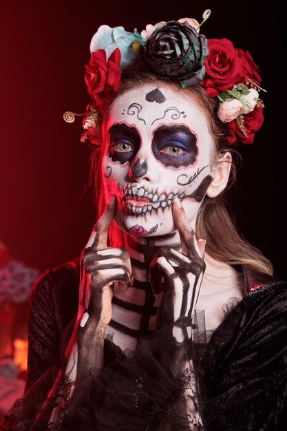 Espeluznante dama de la muerte haciendo cara de beso coqueto en la cámara, con corona de flores y maquillaje de calavera. pareciendo la cavalera catrina o santa muerte, siendo encantador y romántico en dios de los muertos.