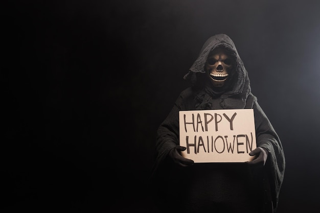 La espeluznante muerte sostiene un cartel de feliz Halloween, muerte con cartel.