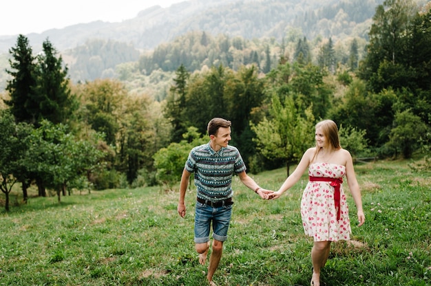 En espera bebé. familia feliz. mujer embarazada con amado esposo caminando sobre la hierba. vientre redondo. Paternidad. Los tiernos momentos sinceros, sonrisas. El marido sostiene a la esposa de la mano. montañas, bosques