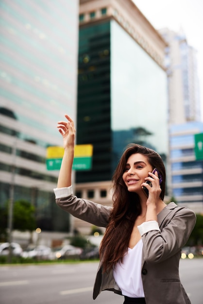 Espera, solo estoy llamando a un taxi Captura recortada de una atractiva joven mujer de negocios llamando a un taxi mientras tomaba una llamada telefónica en la ciudad durante el día