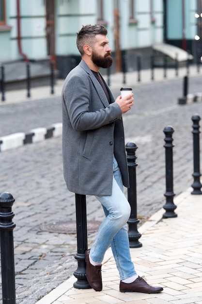 Esperando a alguien en la calle Hombre barbudo hipster beber café taza de papel Empresario bien arreglado disfrutar de un descanso para tomar café al aire libre fondo urbano Disfrutar de la hora del café Camine y disfrute de un café recién hecho