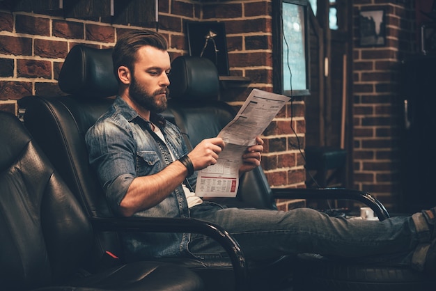 Esperando cita. Hombre barbudo joven guapo leyendo el periódico