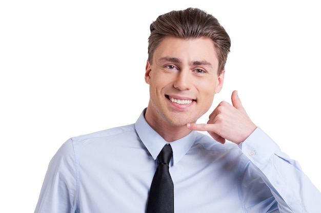 Esperando pela sua ligação! Jovem bonito em trajes formais, gesticulando na placa do telefone e sorrindo enquanto fica de pé, isolado no branco