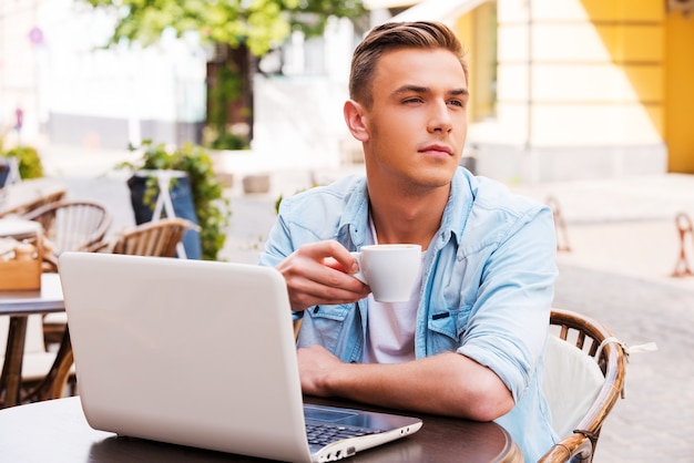 Esperando por amigo. Jovem bonito tomando café enquanto está sentado em um café na calçada