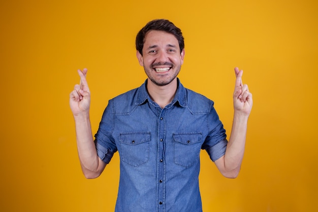 Esperando por um momento especial. retrato de jovem em camisa, mantendo os dedos cruzados sobre fundo amarelo.