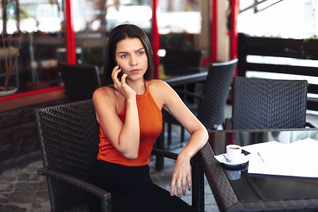 Esperando una reunión, llega tarde a una cita. Una niña sentada con un teléfono en sus manos mira a la pantalla una triste taza de café frente a ella, esperando a su compañero o socio comercial.