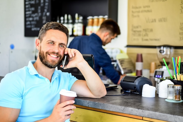 Esperando por ti. Hombre smartphone pedir café en la cafetería. Concepto de pausa para el café. Opción de café para llevar para gente ocupada. Fondo de barista de café de conversación móvil de hombre. Bebe café mientras esperas.