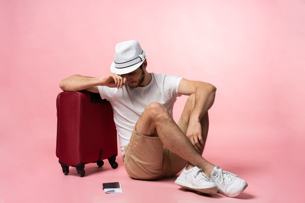 Esperando el vuelo. Viajero hombre sentado en el suelo con maleta.