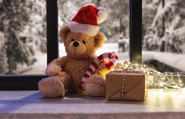 Espere a que el oso de peluche de Santa en el alféizar de una ventana, las luces de Navidad y la caja de regalo, el cálido interior de la casa