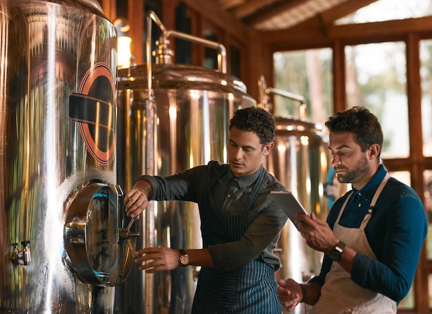 Esperemos que este lote sea bueno Foto de dos jóvenes trabajadores inspeccionando su maquinaria de elaboración de cerveza dentro de una cervecería durante el día