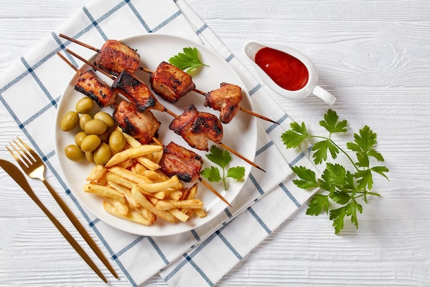 Espetadas de carne de porco grelhadas com batatas fritas num prato