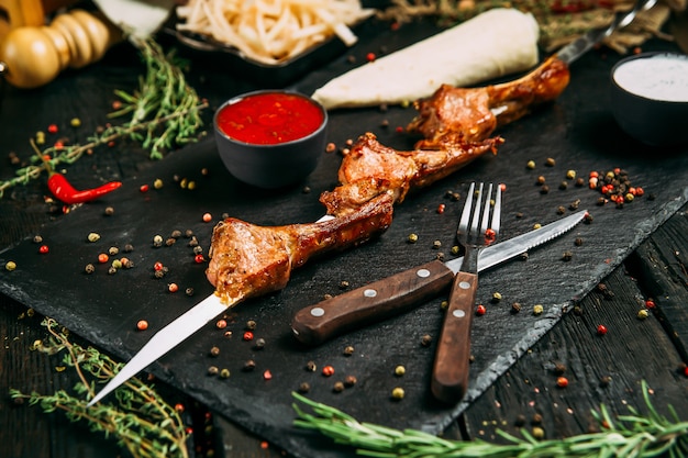 Espetinhos de entrecosto de carne de carneiro apetitosos com molho vermelho e cebola em conserva em um quadro negro