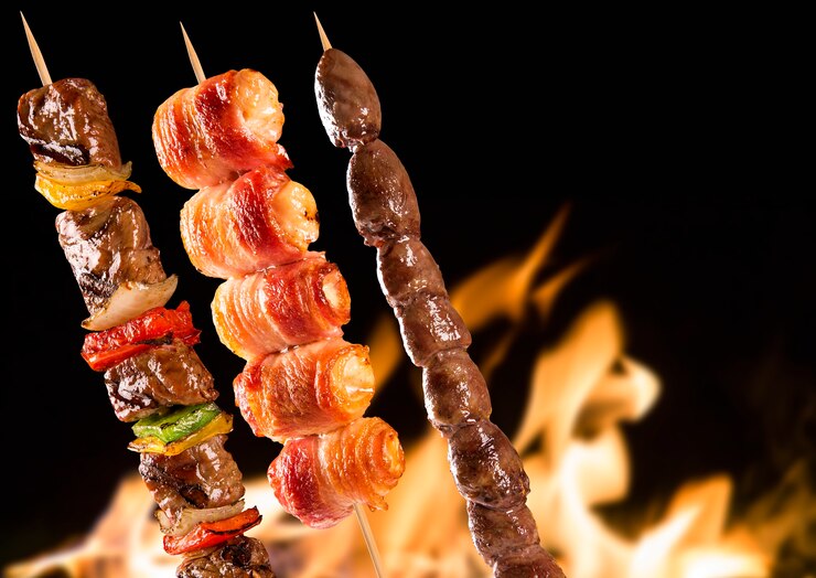Espetos de bife variados sobre chamas de fogo.