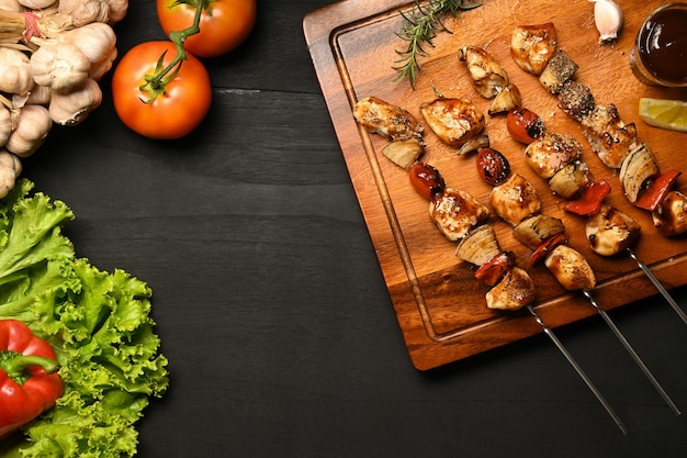 Espetos de carne com legumes grelhados e molho de churrasco em uma tábua de cortar Copie o espaço para o seu texto