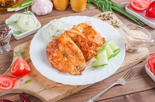 Espetos de carne de frango grelhado com legumes frescos em um prato branco sobre um fundo escuro de madeira