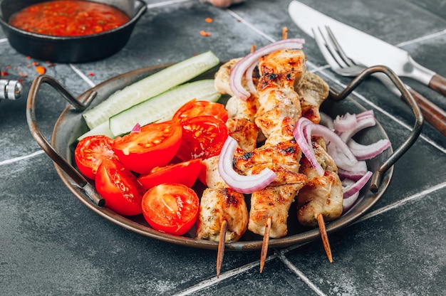 Espetos de frango grelhado com legumes e molho de tomate em fundo de azulejo preto Foco seletivo