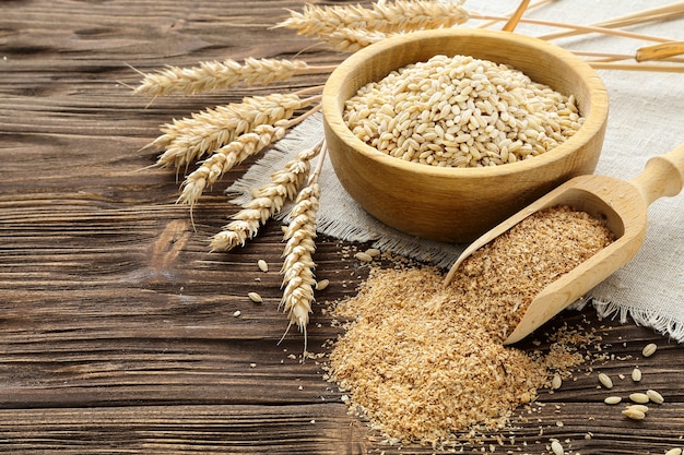 Espigas de farelo, grãos e trigo em uma mesa de madeira marrom