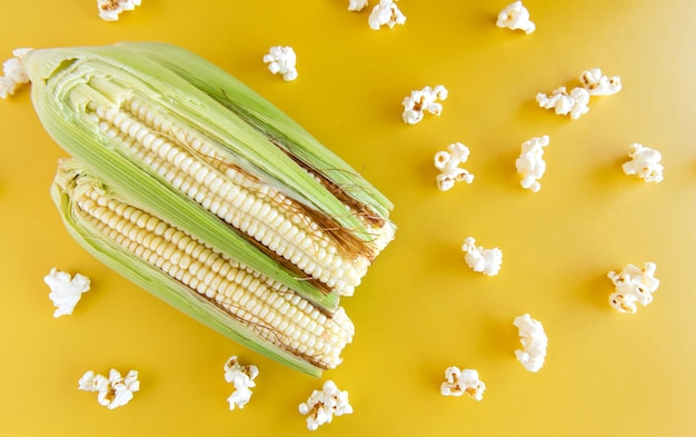 Espigas de milho verde e pipocas em fundo amarelo