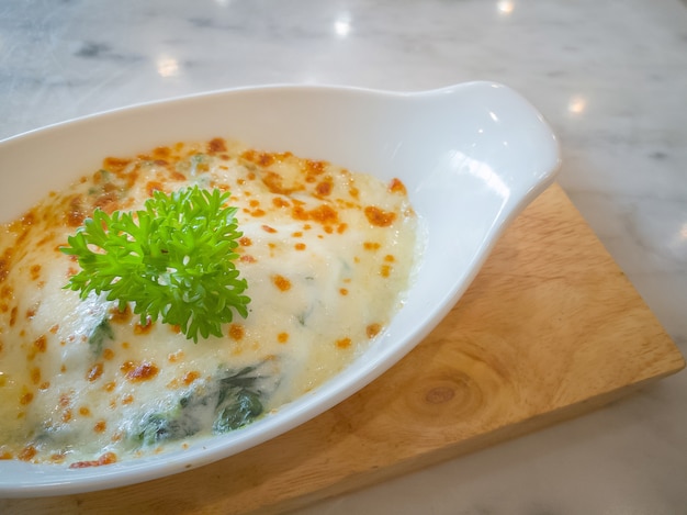 Espinacas con queso en un tazón blanco sobre placa de madera