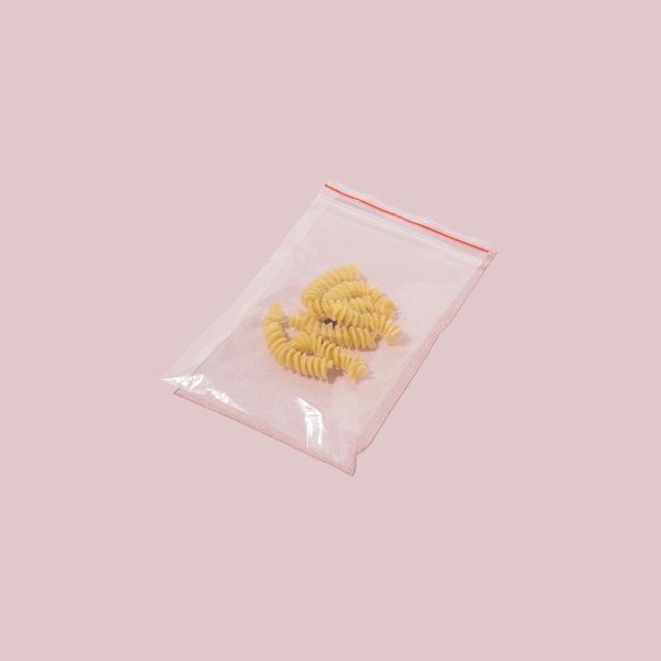 Foto espirais de grãos inteiros amarelos em um pequeno saco plástico em fundo rosa pastel. estilo de conceito de comida mínima.