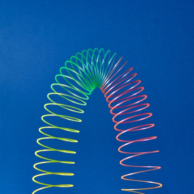 Foto espiral de juguete de colores estratificados en forma de parábola sobre un fondo azul con espacio de copia.