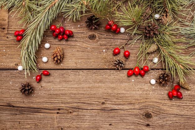 Espírito Natal na mesa de madeira. Bagas frescas de cachorro-rosa, balas, galhos de pinheiro e cones, neve artificial. Decorações da natureza, tábuas de madeira vintage