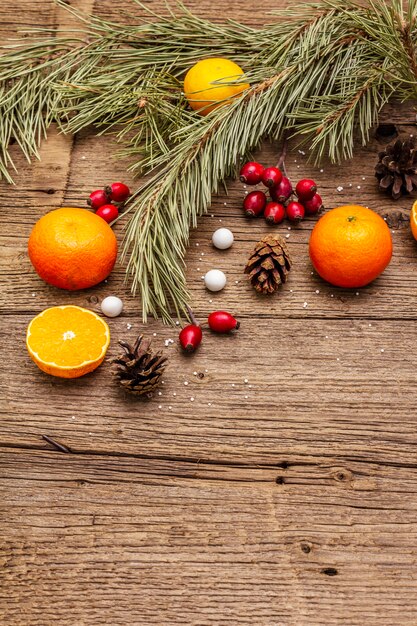 Espírito Natal na mesa de madeira. Tangerinas frescas, bagas de rosas cor de rosa, doces, galhos e cones de pinheiros, neve artificial