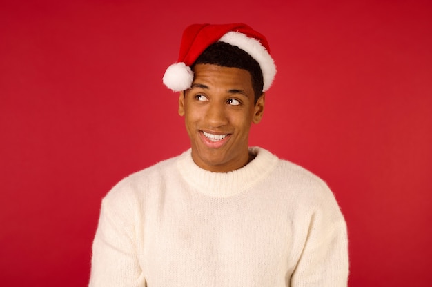 Espíritu navideño. Chico sonriente joven con un suéter blanco y gorro de Papá Noel