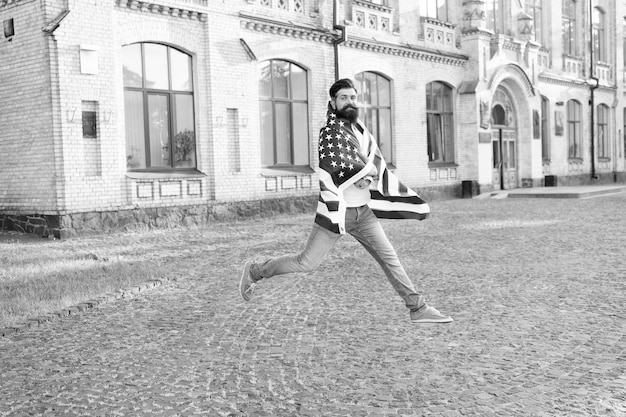 Espíritu patriótico Hombre patriótico saltando con bandera americana Día de la Independencia Ciudadano patriótico hipster barbudo Feliz y orgulloso Únete a la celebración Chico patriótico expresando felicidad en la calle