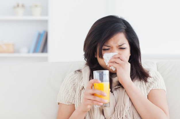 Espirrando uma mulher bebendo um copo de suco de laranja