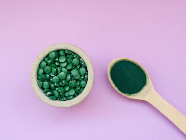 Espirulina havaiana verde em colheres de sopa, pílulas e pó em fundo rosa