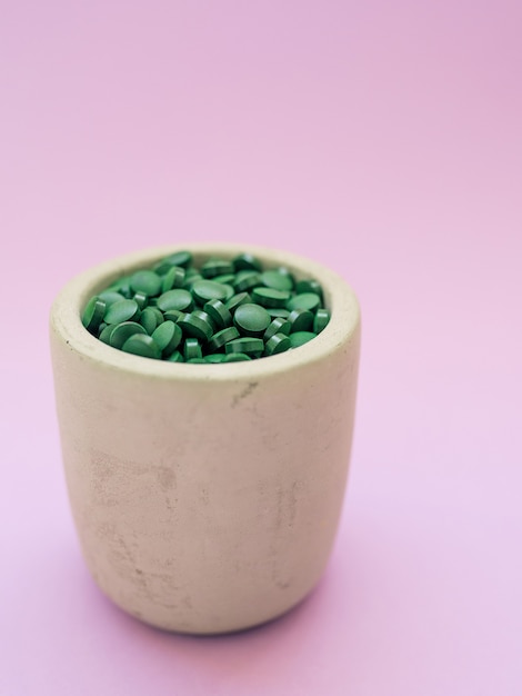 Espirulina havaiana verde em colheres de sopa, pílulas e pó em fundo rosa