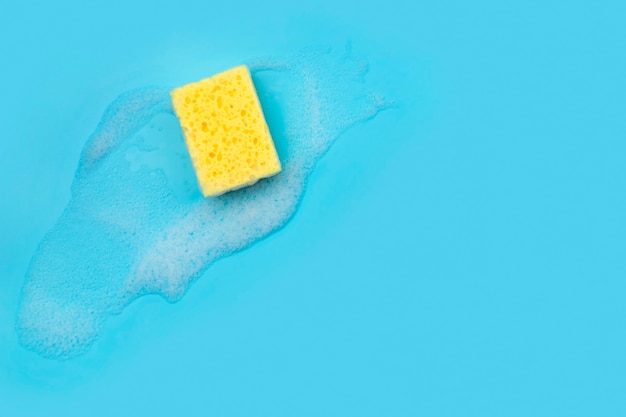 Foto esponja amarela com espuma em fundo azul