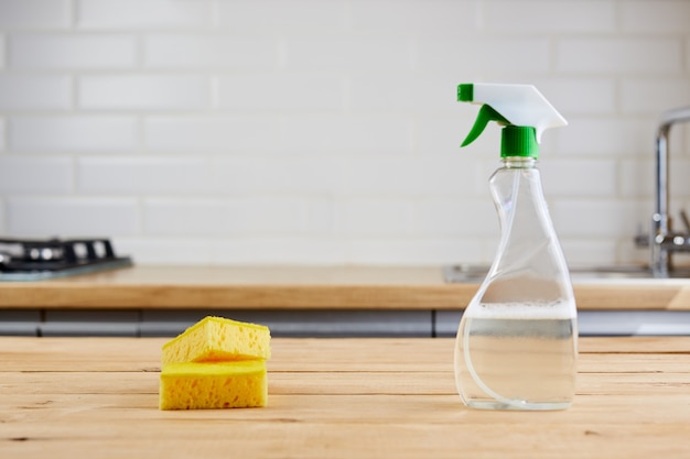 Foto esponja amarilla y botella de plástico con líquido sobre mesa de madera, fondo de cocina