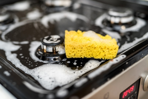 Esponja com espuma no fogão a gás sujo para limpeza. Uma casa limpa é um estilo de vida saudável