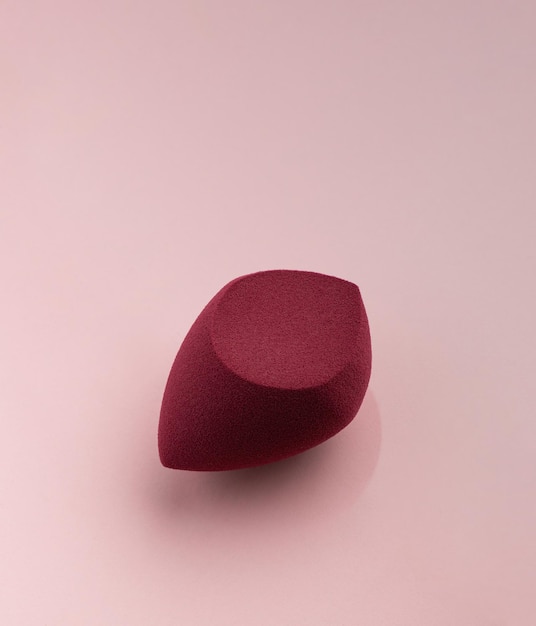 Esponja cosmética vermelha em forma de ovo sobre um fundo rosa