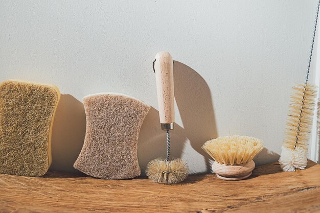 Esponja ecológica, cepillo y cepillo para biberones en una fila contra una pared blanca sobre una superficie de madera. Cero residuos de accesorios limpios. Utensilios naturales de bambú. Limpieza de baños y cocinas en primavera.