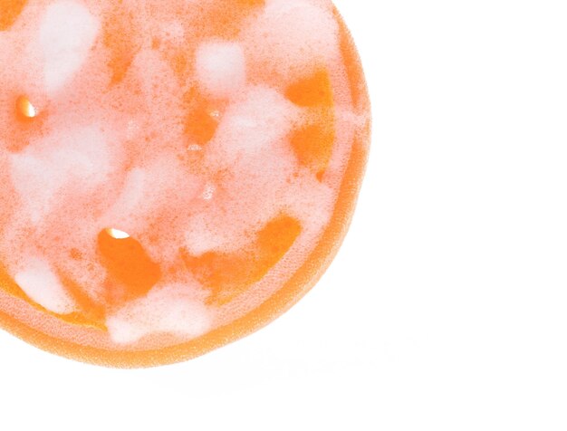 Esponja laranja molhada com espuma isolada no fundo branco.
