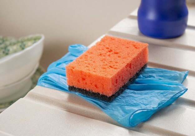 Foto esponja naranja de primer plano para lavar platos y guantes en el borde del fregadero de la cocina
