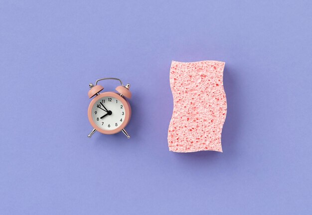 Esponja rosa con despertador sobre fondo púrpura Servicio de limpieza o limpieza diseño creativo
