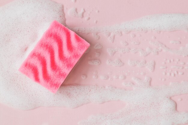 Foto esponja rosa con espuma de detergente sobre fondo rosa de cerca concepto de limpieza