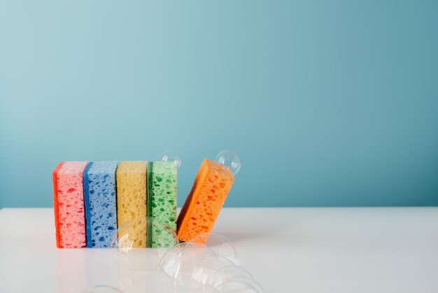 Esponjas de limpeza coloridas com bolhas de sabão na parede azul