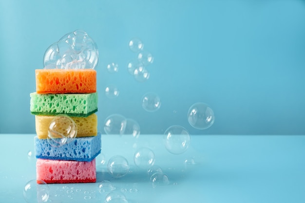 Esponjas de limpieza de colores con pompas de jabón en la pared azul