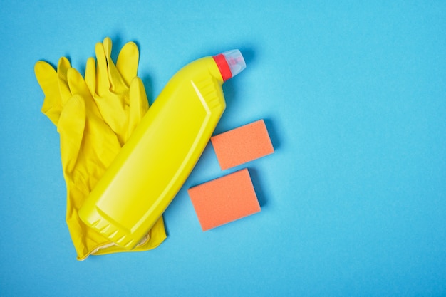 Esponjas, luvas de borracha e frascos de detergente em fundo azul, vista superior, espaço de cópia