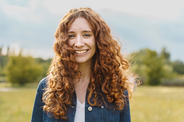 Espontánea mujer pelirroja bastante joven sonriendo mirando a la cámara al aire libre en el retrato de la naturaleza de una chica de cabeza roja en el campo