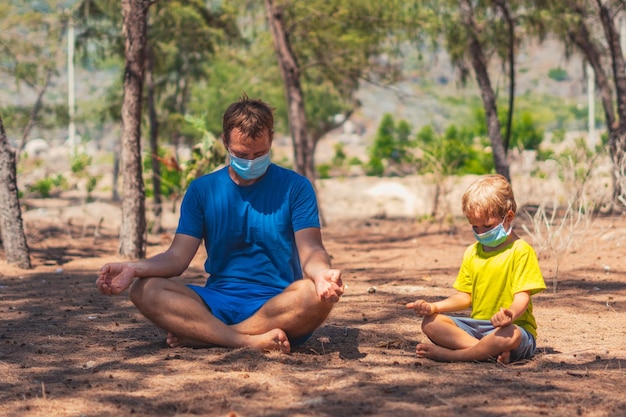 Esporte crianças Pai medita pose de ioga fechar os olhos no parque florestal ar filho repete imitar comportamento usar rosto máscara azul proteger coronavírus andar natureza dia de sol Papai influência na visão de mundo do menino